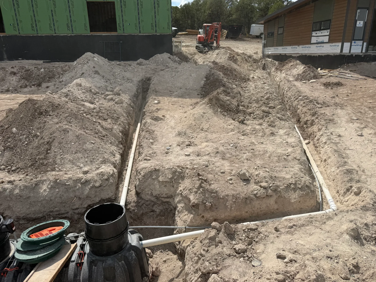 Dual concrete septic tanks with white PVC piping in excavated trenches