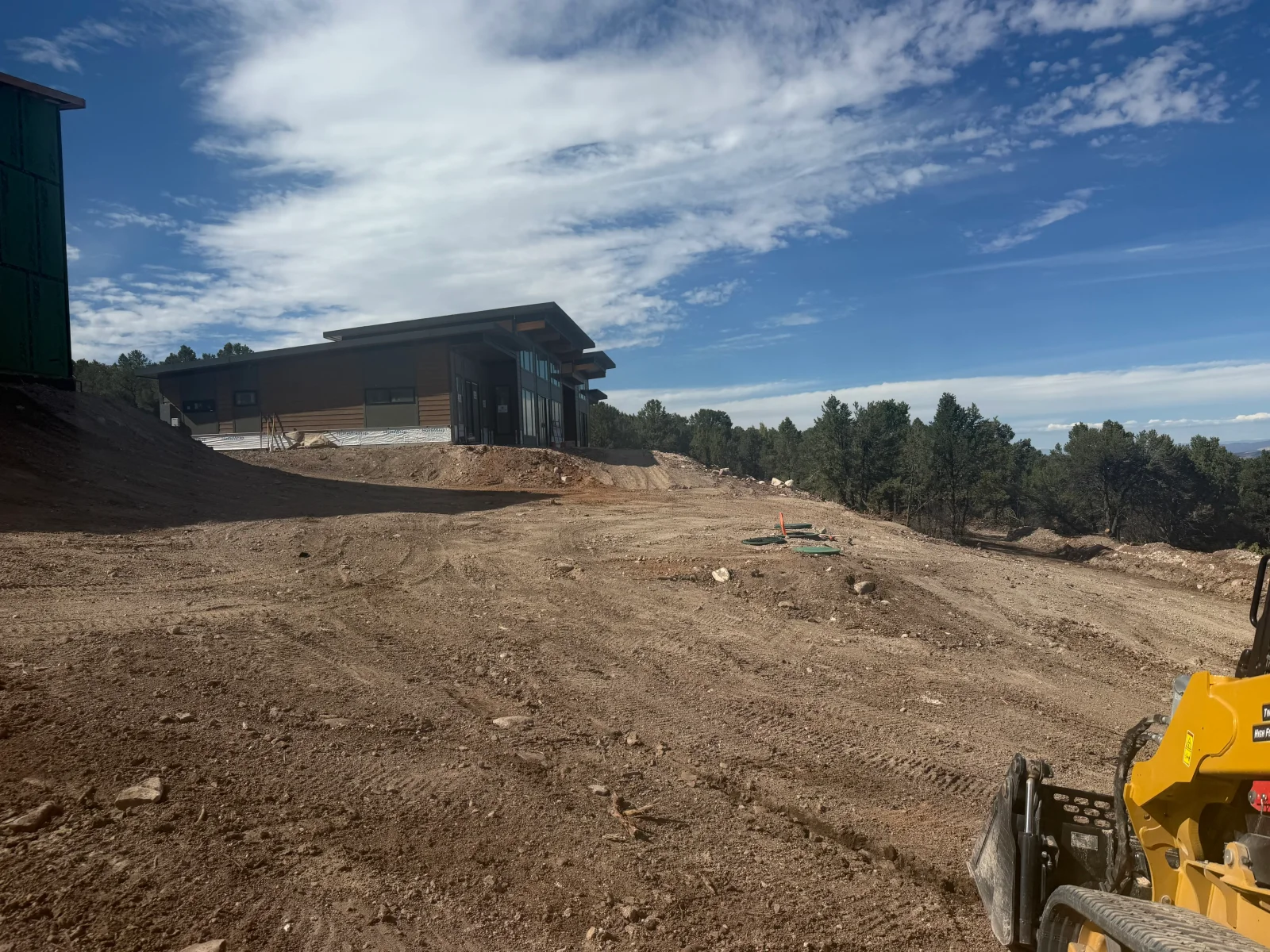 Excavated building site with graded dirt pad, heavy equipment, and modern home foundation in progress