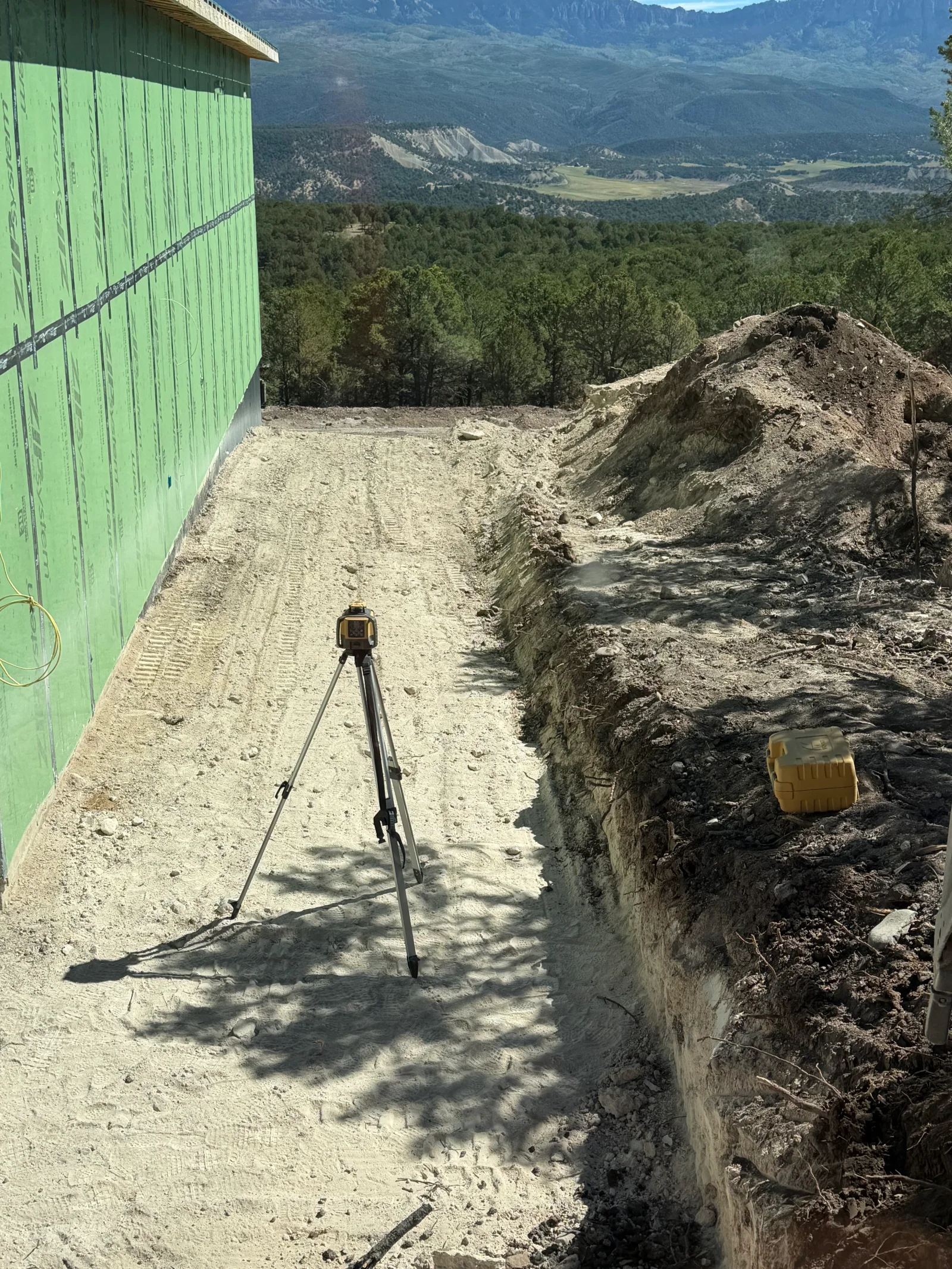 Surveying tripod on graded dirt pad with excavated hillside slope and exposed soil layers